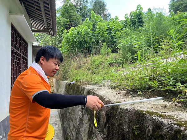 《實測實量》。7月29日，川東南勘察公司駐守地質(zhì)工程師曹志遠在黔江區(qū)阿蓬江鎮(zhèn)分水村，對陸家河滑坡范圍內(nèi)的居民房屋后邊坡已建擋墻的寬度進行實測。王龍貴攝